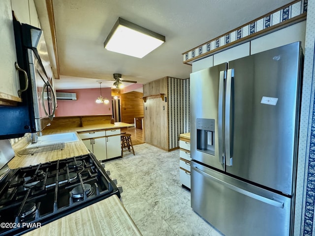 kitchen featuring stainless steel fridge with ice dispenser, kitchen peninsula, wood walls, decorative light fixtures, and white cabinets