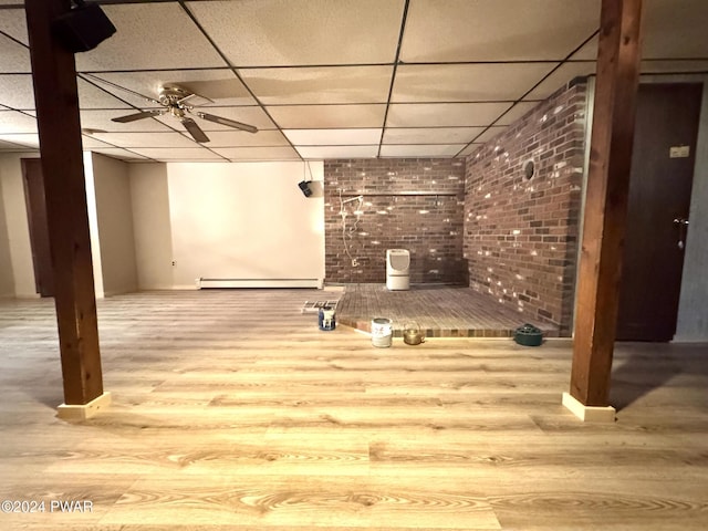 basement with ceiling fan, a drop ceiling, light hardwood / wood-style flooring, and a baseboard heating unit