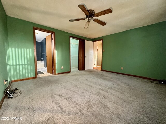 unfurnished bedroom with carpet flooring, ensuite bathroom, ceiling fan, a spacious closet, and a closet