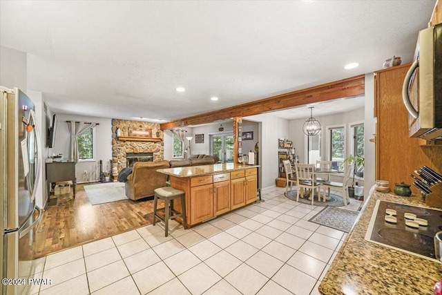 kitchen featuring hanging light fixtures, a kitchen breakfast bar, a stone fireplace, stainless steel fridge, and light tile patterned floors