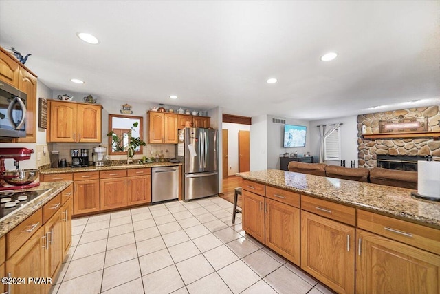 kitchen with decorative backsplash, light stone countertops, a fireplace, appliances with stainless steel finishes, and light tile patterned flooring