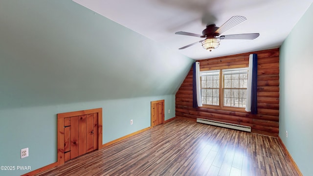 additional living space featuring baseboard heating, wood-type flooring, rustic walls, and vaulted ceiling