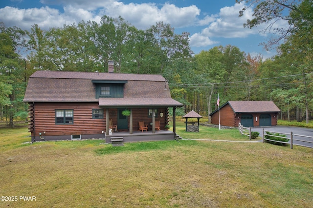 rear view of property featuring a garage, a porch, a yard, and an outbuilding