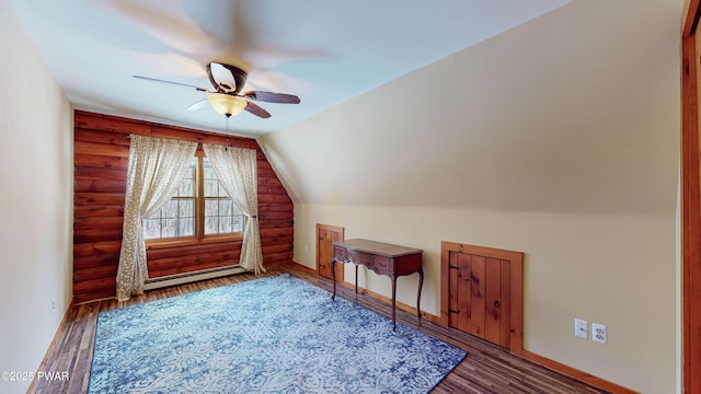 additional living space with lofted ceiling, dark wood-type flooring, rustic walls, ceiling fan, and a baseboard radiator