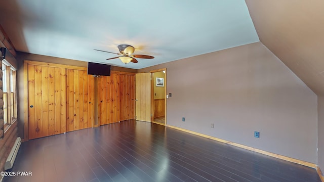 empty room featuring dark hardwood / wood-style flooring, a baseboard radiator, ceiling fan, and wood walls