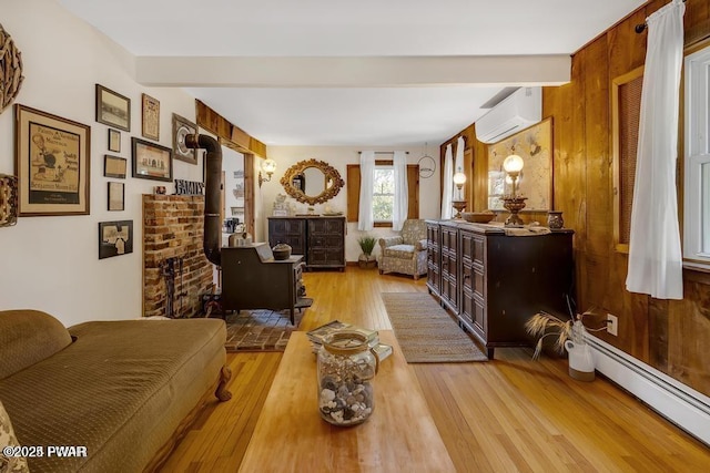 interior space featuring light wood-type flooring, a wood stove, an AC wall unit, beamed ceiling, and a baseboard heating unit