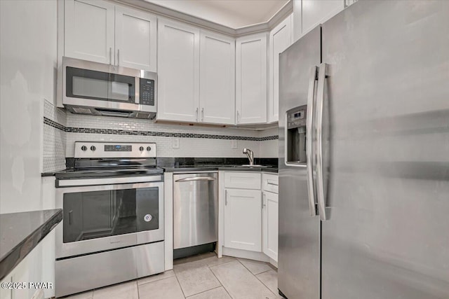 kitchen with tasteful backsplash, light tile patterned floors, stainless steel appliances, white cabinetry, and a sink