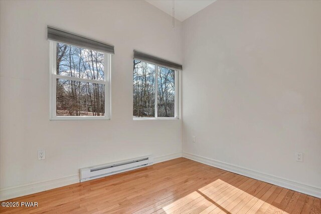 spare room with a baseboard heating unit, plenty of natural light, baseboards, and hardwood / wood-style floors