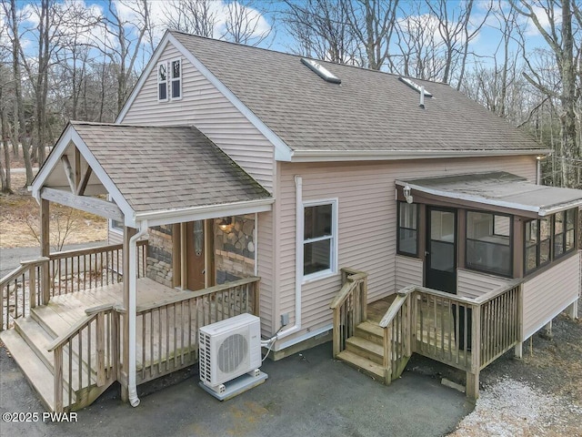 rear view of house featuring a wooden deck, roof with shingles, ac unit, a sunroom, and stone siding