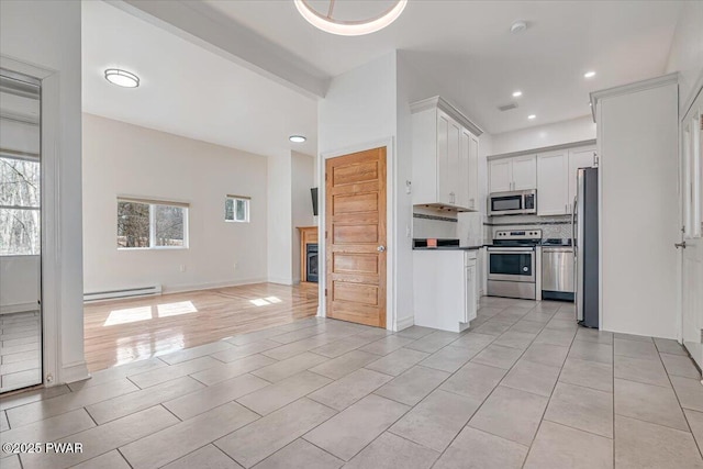 kitchen featuring backsplash, open floor plan, baseboard heating, appliances with stainless steel finishes, and white cabinetry