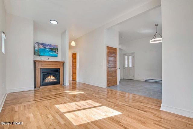 unfurnished living room with a glass covered fireplace, a baseboard heating unit, baseboards, and wood finished floors