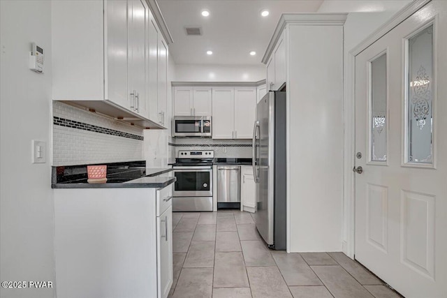 kitchen with light tile patterned floors, visible vents, stainless steel appliances, decorative backsplash, and dark countertops