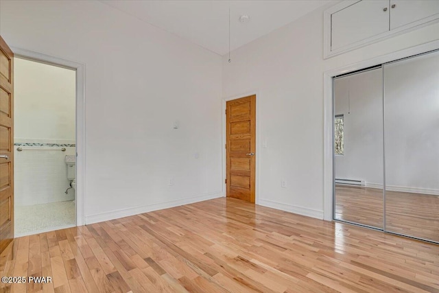 unfurnished bedroom featuring a baseboard heating unit, a closet, connected bathroom, light wood finished floors, and baseboards