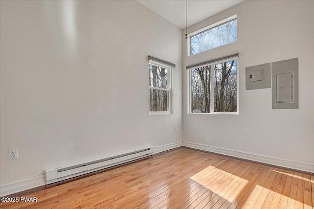 empty room featuring hardwood / wood-style flooring, electric panel, baseboards, and baseboard heating