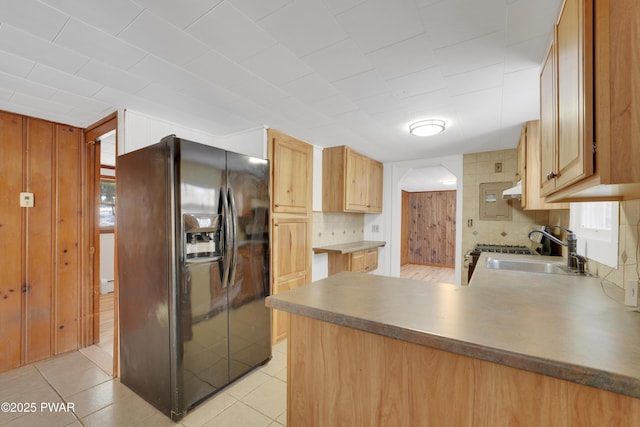 kitchen with light tile patterned flooring, sink, black fridge, kitchen peninsula, and backsplash