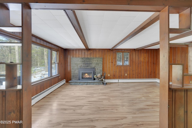 unfurnished living room with a stone fireplace, wooden walls, beamed ceiling, a baseboard heating unit, and light hardwood / wood-style flooring