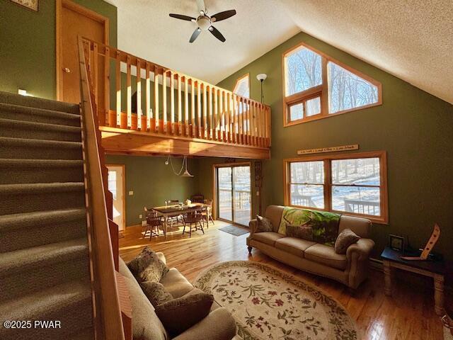 living room with hardwood / wood-style flooring, ceiling fan, high vaulted ceiling, and a textured ceiling