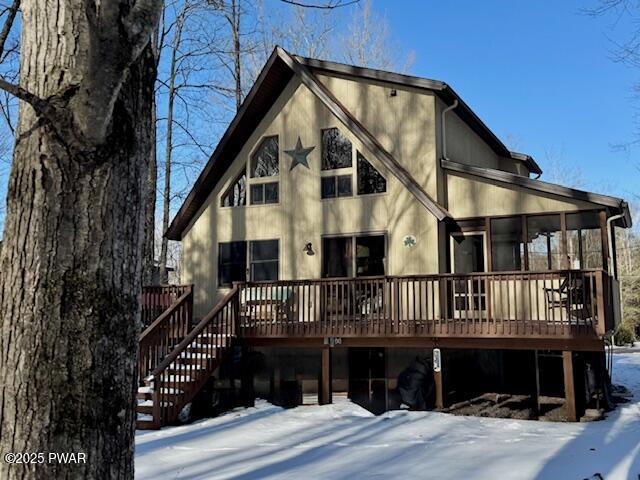 snow covered back of property with a wooden deck