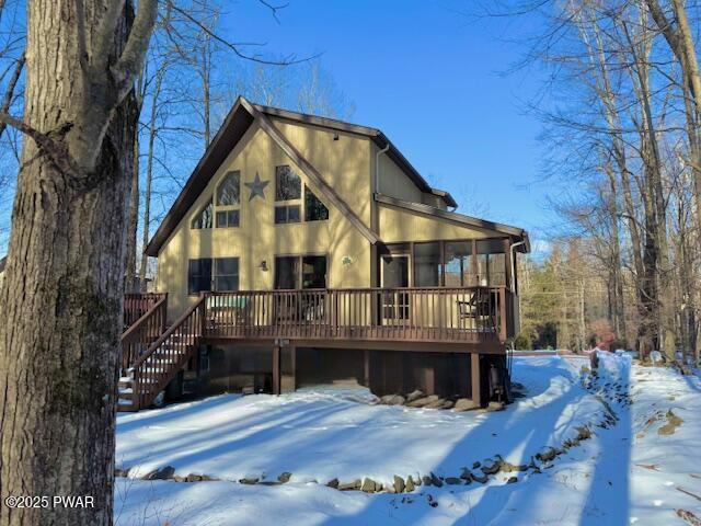 snow covered house featuring a deck and a sunroom