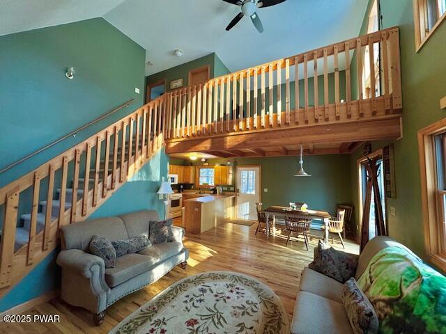 living room with ceiling fan, high vaulted ceiling, and light hardwood / wood-style flooring