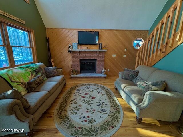 living room with lofted ceiling, wooden walls, light hardwood / wood-style floors, and a brick fireplace