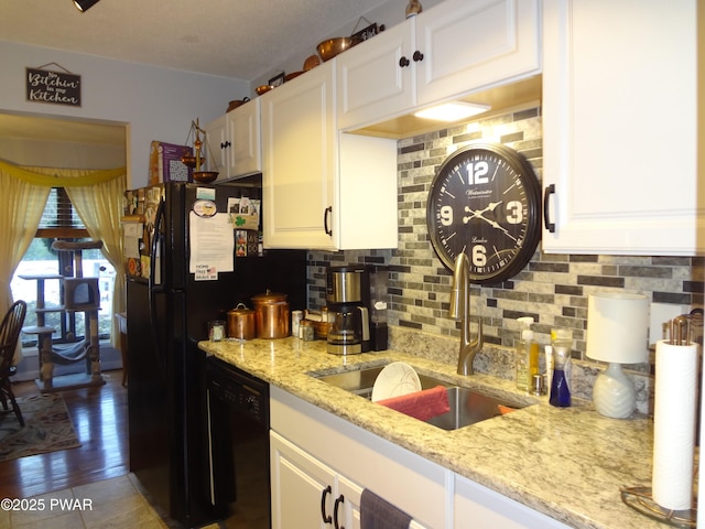 kitchen with sink, light stone counters, black dishwasher, and white cabinetry