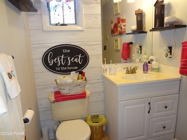 bathroom featuring toilet, vanity, and wooden walls