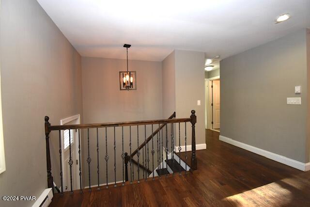 staircase featuring hardwood / wood-style flooring, a baseboard heating unit, and a notable chandelier