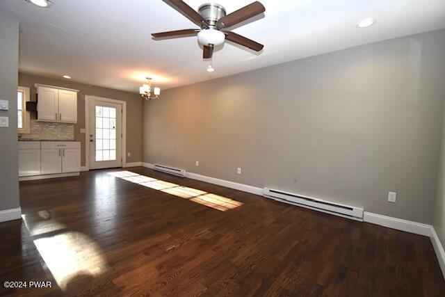 unfurnished living room featuring ceiling fan with notable chandelier, baseboard heating, and dark wood-type flooring