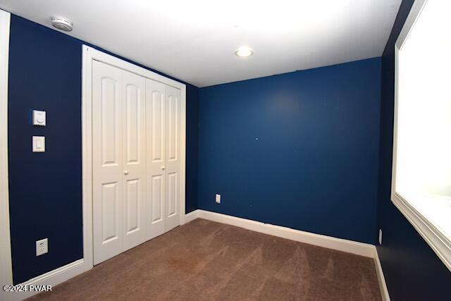 unfurnished bedroom with dark colored carpet and a closet