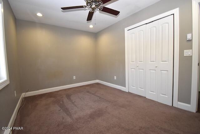 unfurnished bedroom with ceiling fan, dark carpet, and a closet