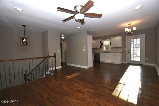 empty room featuring ceiling fan with notable chandelier, sink, and dark wood-type flooring