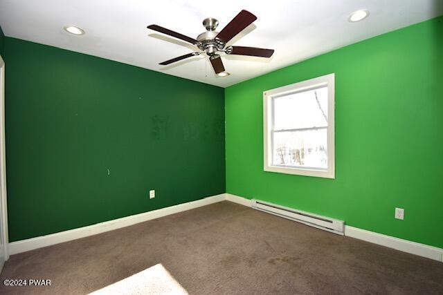 carpeted spare room featuring baseboard heating and ceiling fan