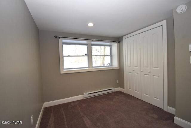 unfurnished bedroom featuring dark carpet, a closet, and a baseboard heating unit