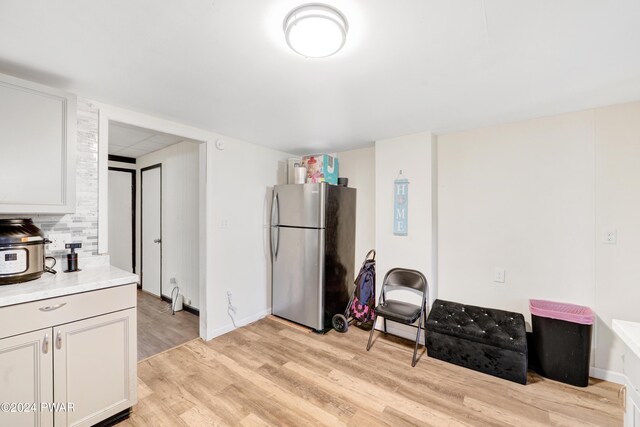 kitchen with tasteful backsplash, stainless steel refrigerator, white cabinetry, and light hardwood / wood-style floors