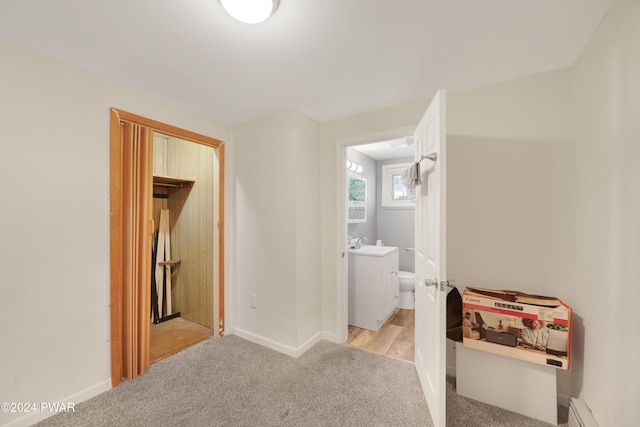 corridor with sink, light colored carpet, and baseboard heating