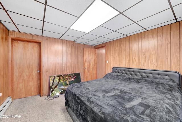 carpeted bedroom featuring a paneled ceiling, a closet, wood walls, and a baseboard heating unit