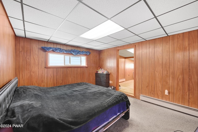 bedroom featuring carpet, a paneled ceiling, a baseboard heating unit, and wood walls