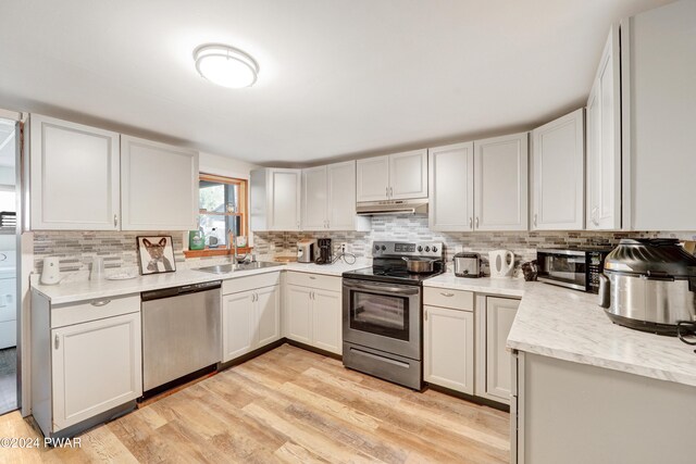 kitchen featuring backsplash, sink, light wood-type flooring, white cabinetry, and stainless steel appliances