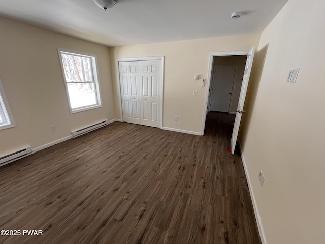 unfurnished bedroom with baseboards, a baseboard heating unit, dark wood finished floors, and a closet