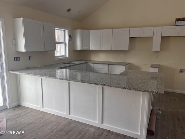 kitchen with kitchen peninsula, light stone countertops, vaulted ceiling, pendant lighting, and white cabinets