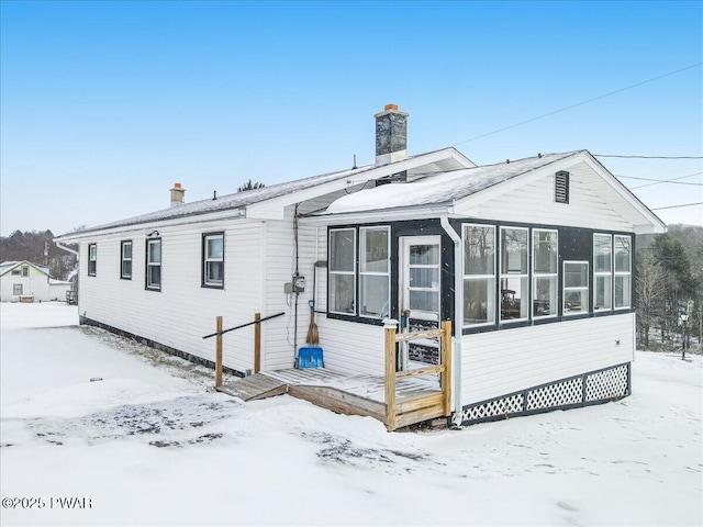 snow covered rear of property featuring a sunroom