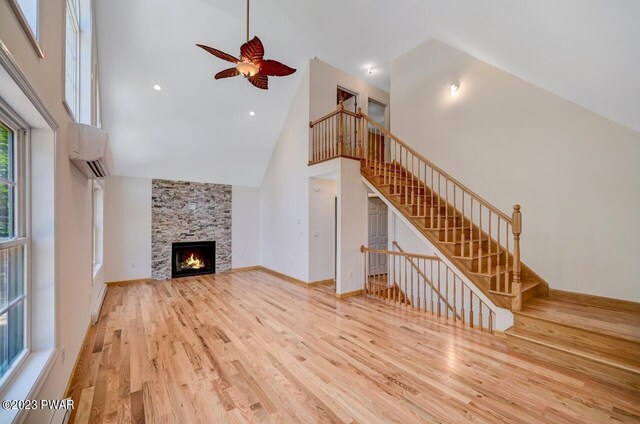 unfurnished living room featuring high vaulted ceiling, light hardwood / wood-style flooring, ceiling fan, a fireplace, and a wall mounted AC