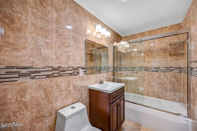 full bathroom with vanity, toilet, tile walls, and bath / shower combo with glass door