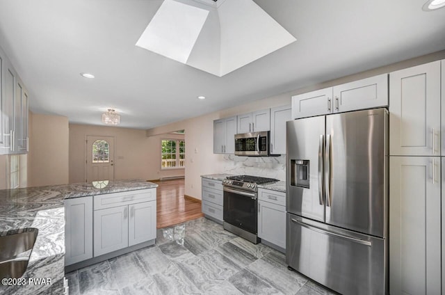 kitchen with light stone countertops, gray cabinets, a skylight, and stainless steel appliances