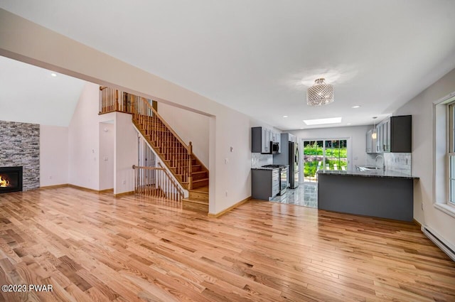 unfurnished living room featuring vaulted ceiling, a baseboard heating unit, sink, light hardwood / wood-style flooring, and a stone fireplace