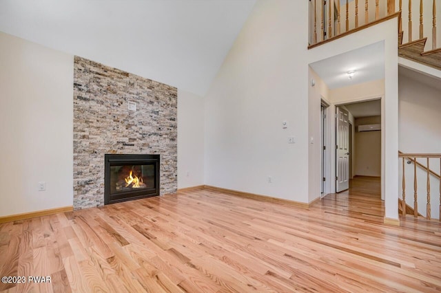 unfurnished living room featuring an AC wall unit, a stone fireplace, light hardwood / wood-style flooring, and high vaulted ceiling