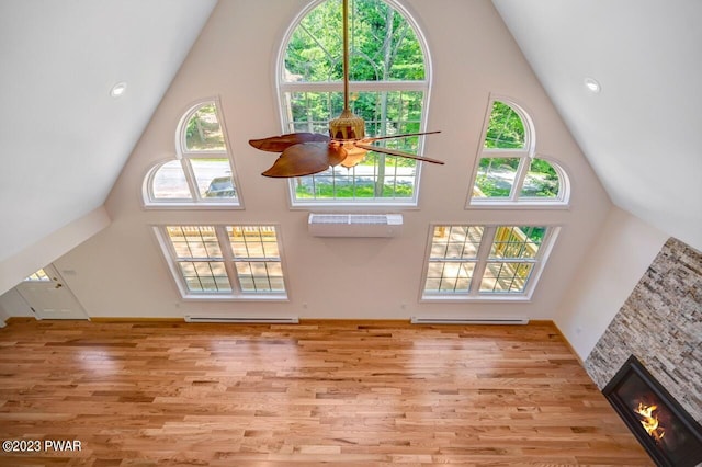 unfurnished living room featuring a high ceiling, light wood-type flooring, a stone fireplace, and ceiling fan