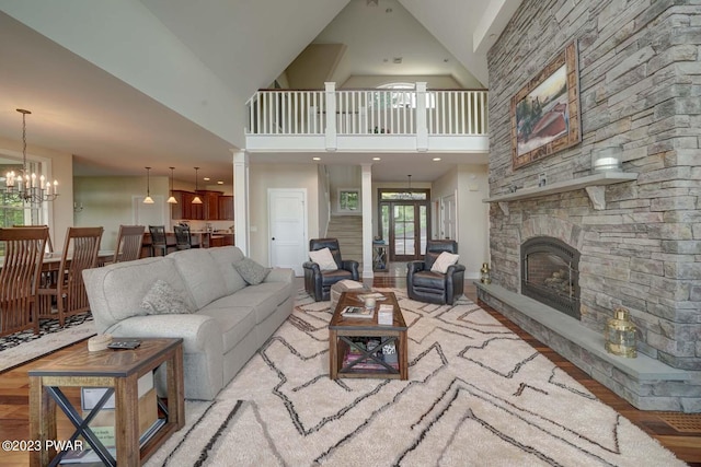 living room featuring a chandelier, light hardwood / wood-style flooring, high vaulted ceiling, and a stone fireplace