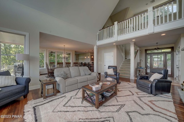 living room featuring hardwood / wood-style floors, ornate columns, high vaulted ceiling, and an inviting chandelier